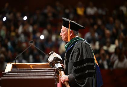 Faculty member holding college mace on stage at commencement ceremony