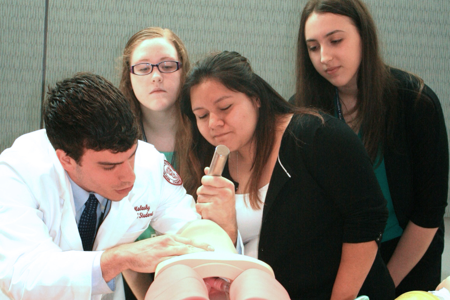 Three students watch as medical professional practices intubation on a manikin