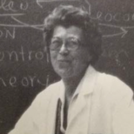 Black and white photo of Johanna Hagedoorn, Ph.D. in a white coat smiling in front of a chalk board.