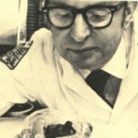 Milton Tabachnick, Ph.D. in white coat examining item.