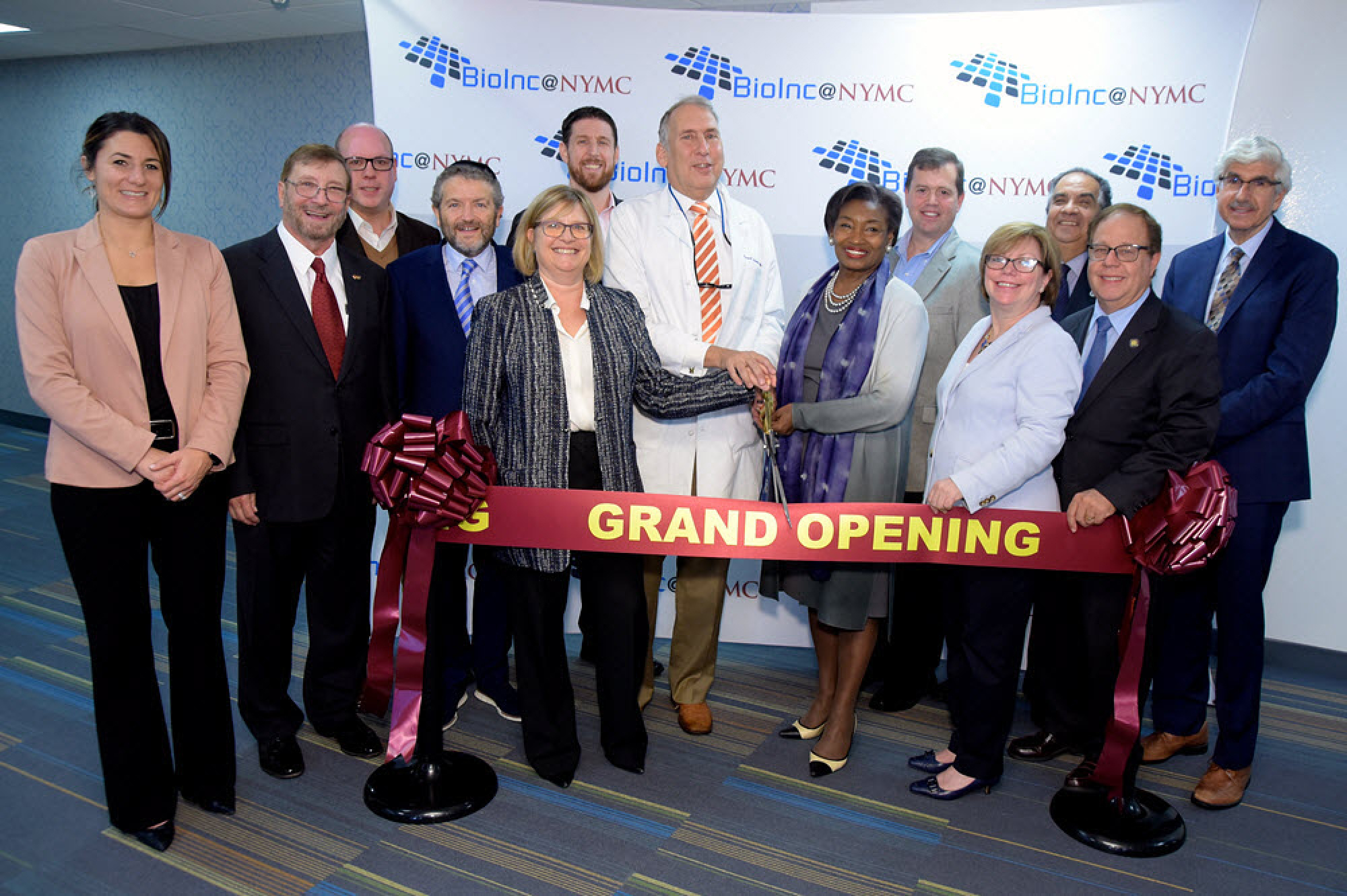 NYMC faculty smiling with grand opening ribbon at BioInc@NYMC grand opening event