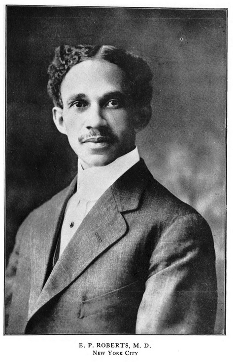 Portrait of Eugene Percy Roberts, a black man with short curly hair, a short mustache, a white shirt with the collar covering his neck, and a blazer. He has neutral expression on face.