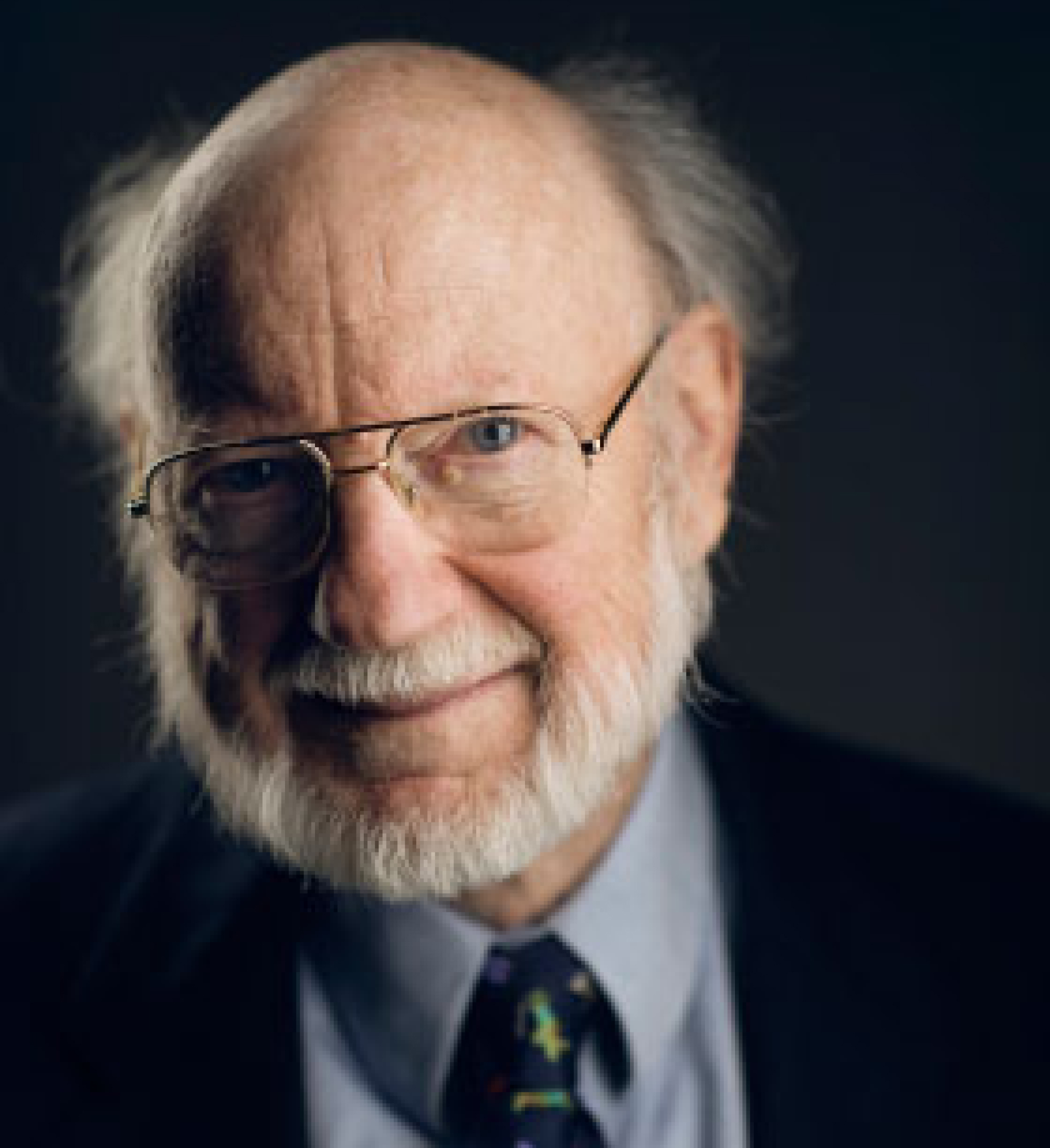 William Campbell with gray hair, blue eyes, and aviator eyeglasses, wearing a suit and a tie