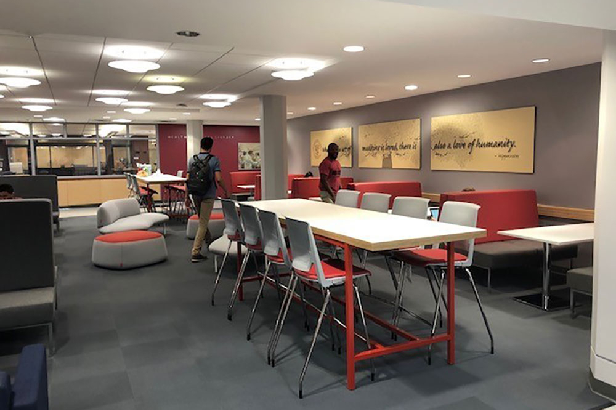 Hales lobby with gray carpet, large tables and booths with gray and red seating, and wall art with inspirational quote