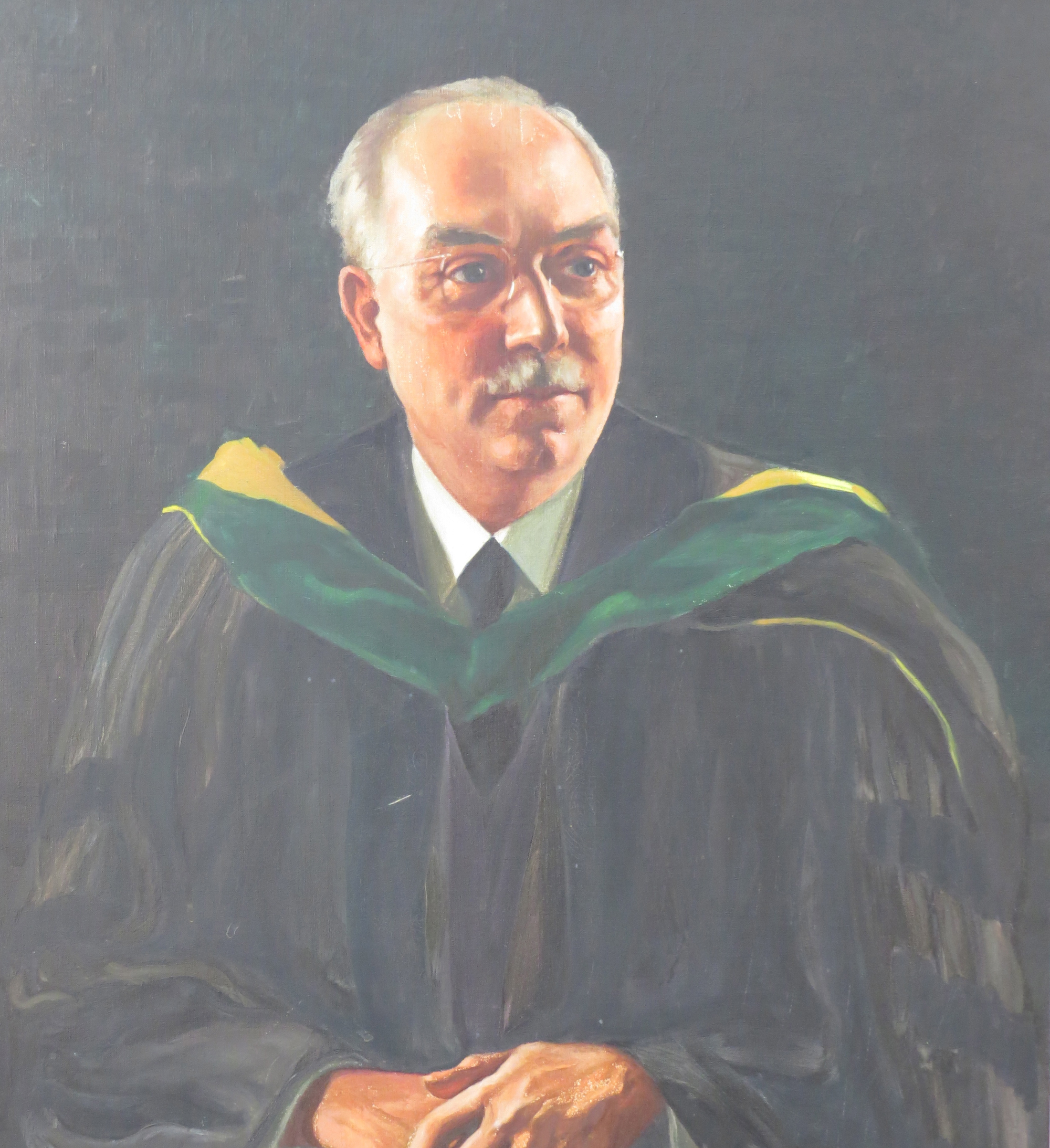 J.A.W. Hetrick portrait. Light skin, short and thin gray hair, thick eyebrows, a neat gray mustache, thin glasses, and a green and black robe