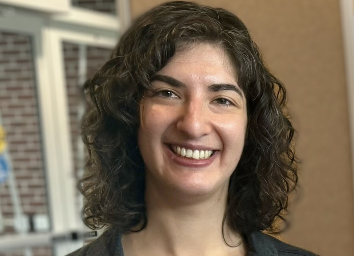 Woman with short curly hair smiling inside a building.