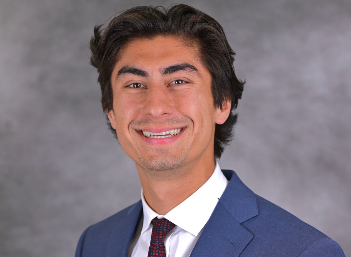 Man with short hair smiling wearing a suit.