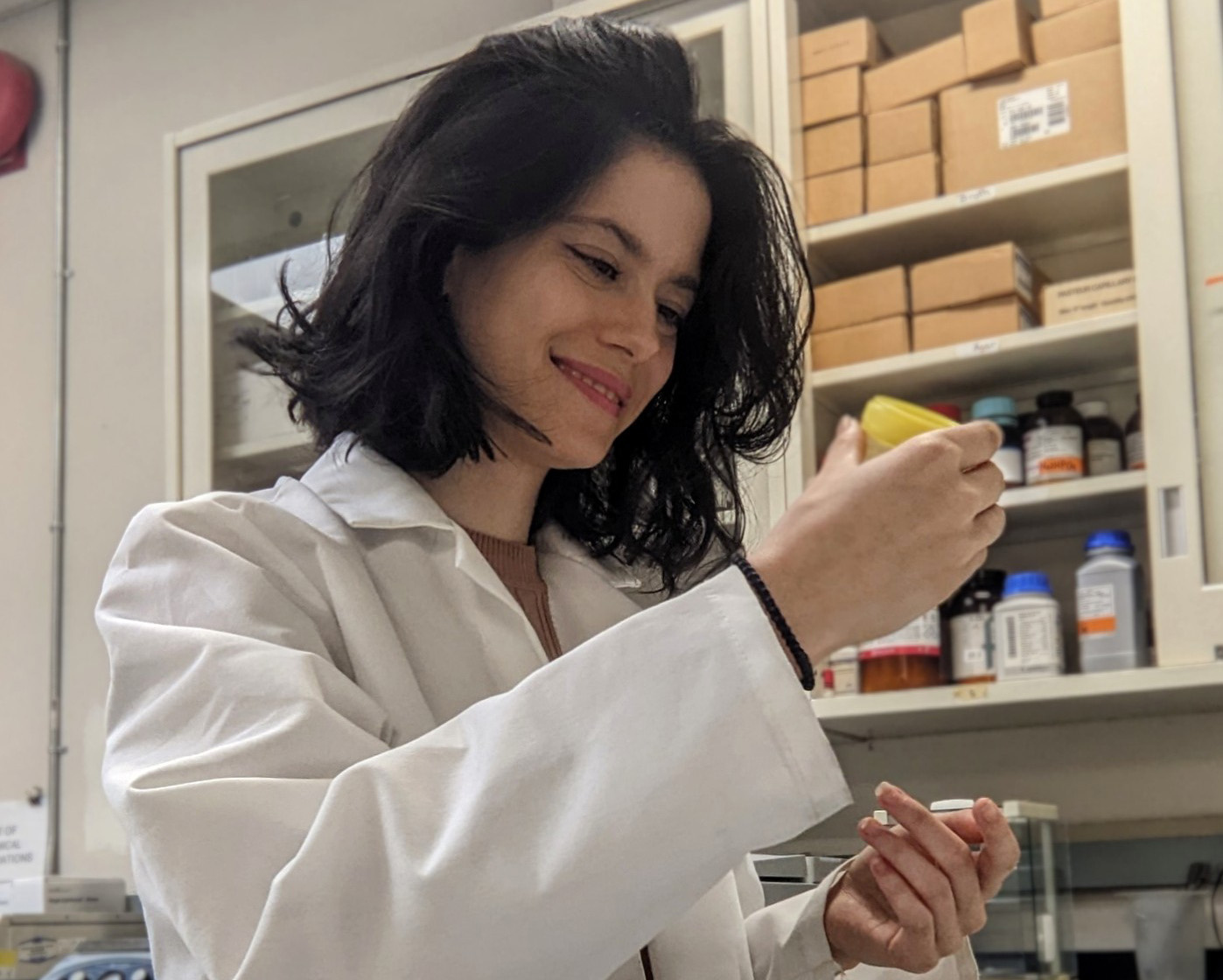 Female medical student wearing a white coat in a lab looking at a specimen in a container.