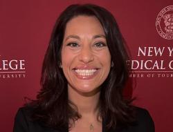 Woman with dark brown hair to her shoulders smiling in front of a maroon New York Medical College banner with white lettering