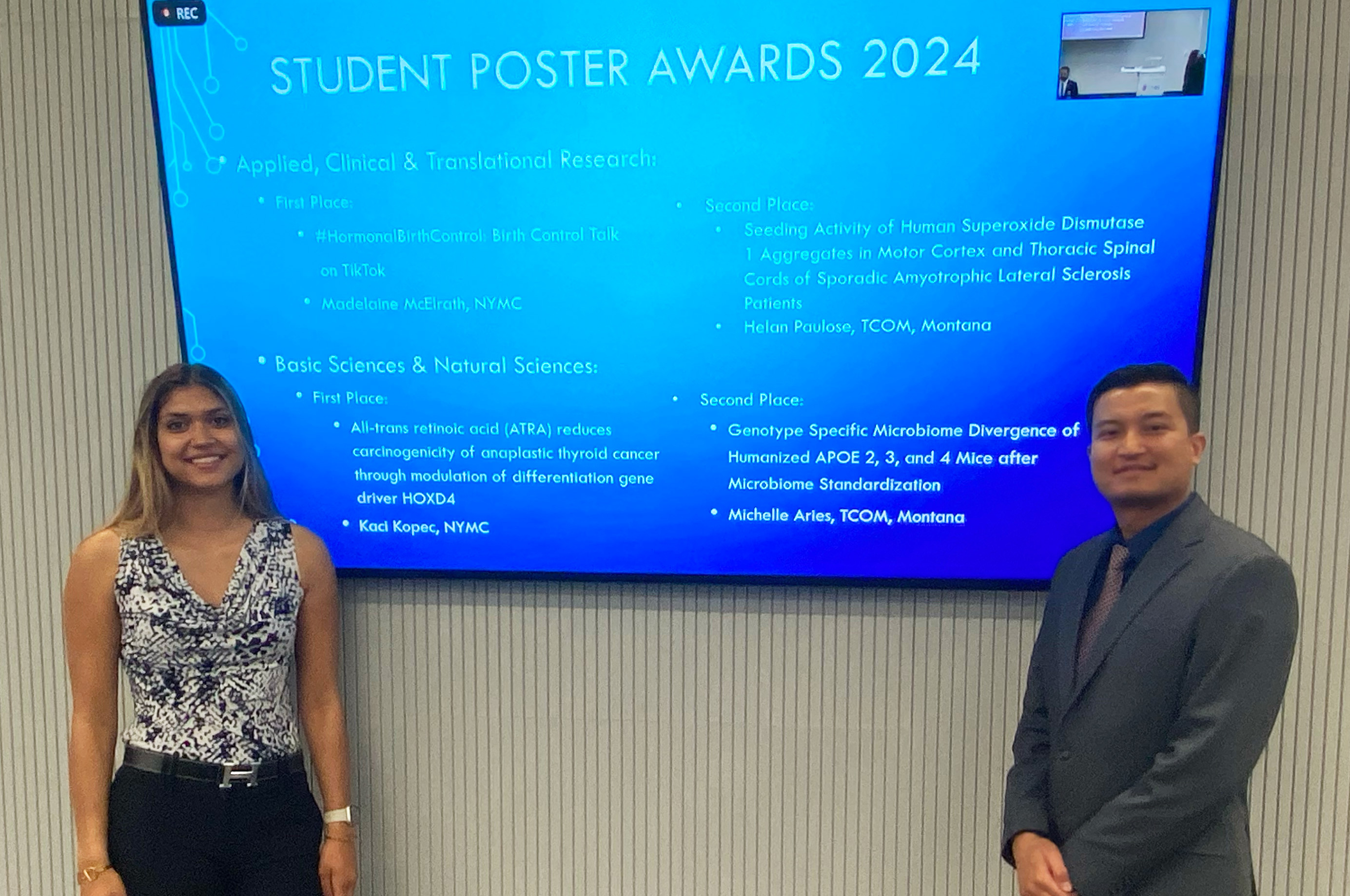 Two students standing in front of a screen for poster presentations.