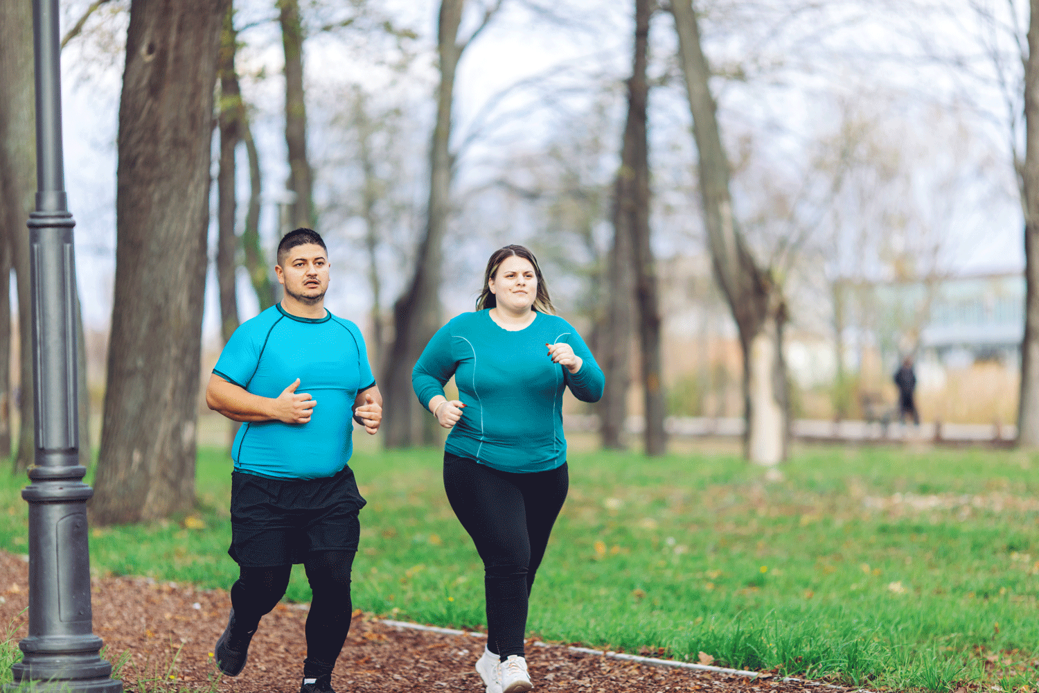 two overweight individuals, a man on the left and a woman on the right, running in a park.