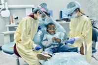 a child sitting on a doctors chair surrounded by two student dentists