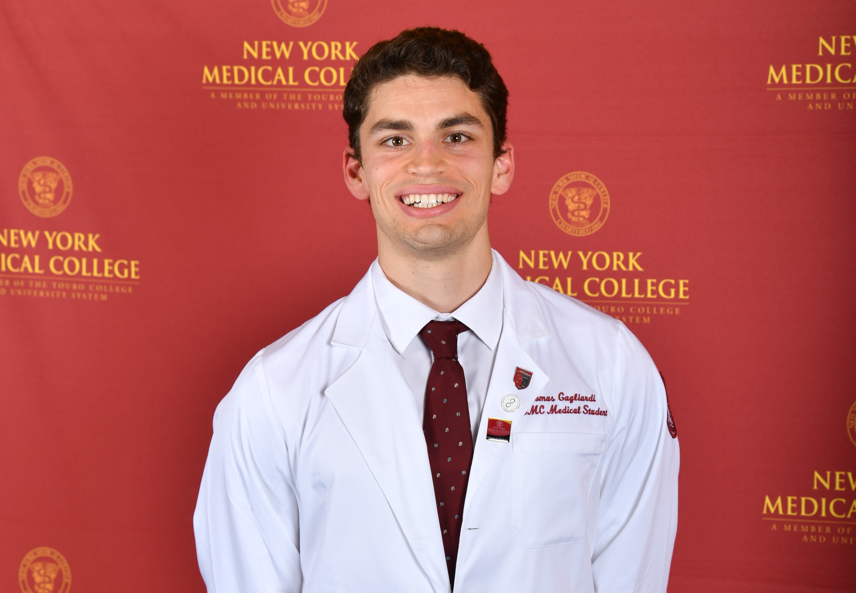 Thomas Gagliardi, SOM Class of 2024, standing in front of the College step and repeat banner