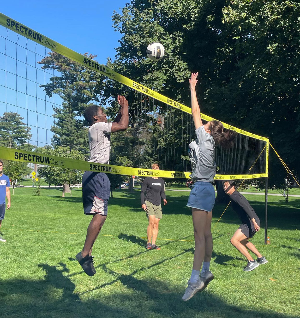 Students leaping to hit the ball while playing a game of volleyball on campus