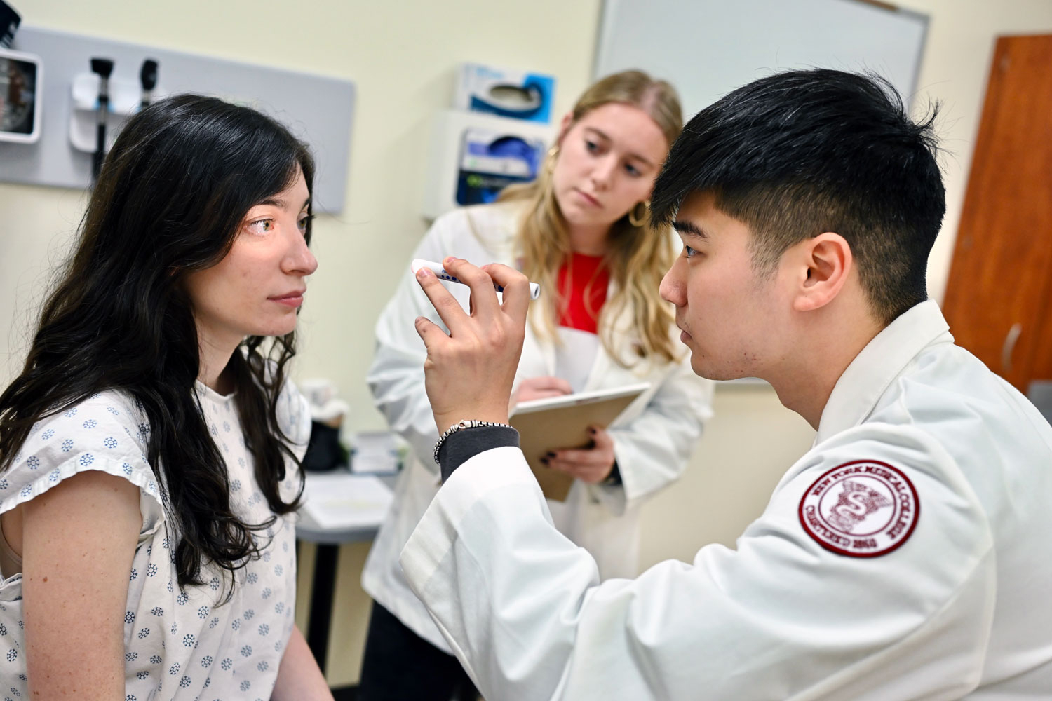 Student shining light in patient's eyes while other student watches